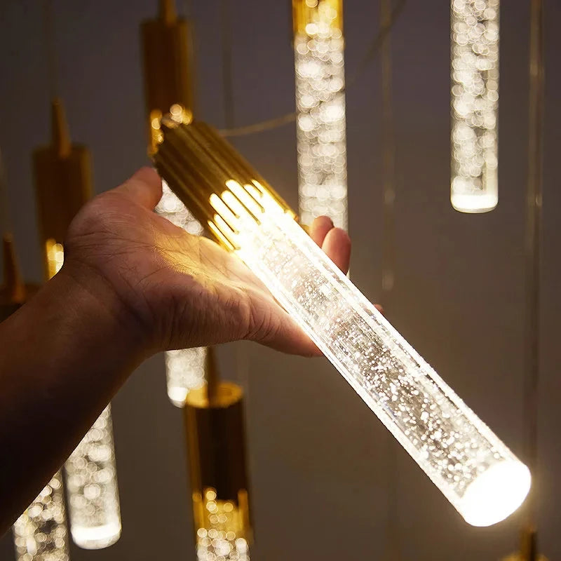 Tube lumineux suspendu en cristal transparent avec finition dorée.